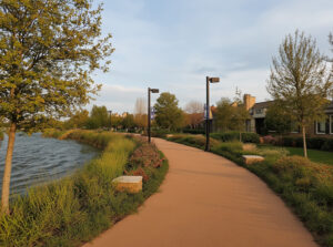 Paseo peatonal ribereño al atardecer: camino curvo, lago tranquilo, árboles y vegetación natural en barrio privado