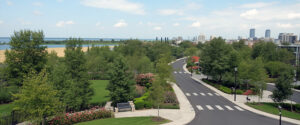 Vista aérea panorámica de parque urbano con caminos curvos, bancos, árboles frondosos, rosales y horizonte con río y skyline de ciudad, diseño paisajístico integrado para desarrollos residenciales en Patagonia, Lineasur Arquitectos Cipolletti Río Negro.