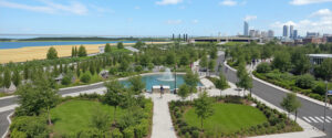 Vista aérea de parque urbano moderno con fuente central en plaza circular, caminos peatonales, árboles frondosos, áreas verdes y horizonte con río, puente y skyline de ciudad, referencia paisajística para desarrollos residenciales en Patagonia Norte, Lineasur Arquitectos Cipolletti Río Negro.