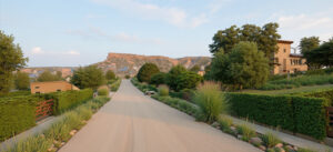 Calle interna residencial al atardecer – Proyecto ribereño Cipolletti, Río Negro. Trazado curvo con vegetación nativa, setos y vistas a las mesetas patagónicas